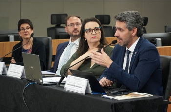 Palestrantes participam de mesa-redonda em auditório, com notebooks e microfones sobre a mesa.