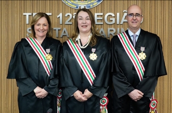 A imagem mostra duas magistradas e um magistrado posando lado a lado, usando togas pretas e faixas nas cores verde, branca e vermelha, com medalhas douradas presas ao peito.