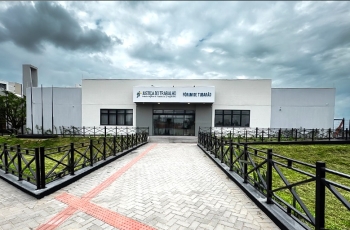 Prédio térreo em cor cimento queimado, ladeado por dois gramados. Céu nublado