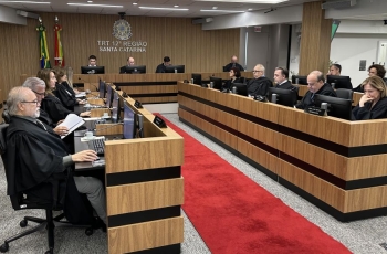Sala de sessões de um tribunal mostrando 19 pessoas sentadas em uma mesa em formato de U