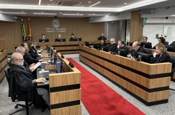 Sala de sessões de um tribunal mostrando 19 pessoas sentadas em uma mesa em formato de U