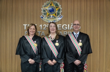 Três pessoas usando toga, uma faixa em torno dela e uma medalha fixada na toga