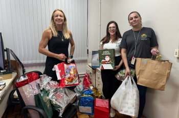 Foto de três mulheres exibindo presentes que foram entregues à entidade