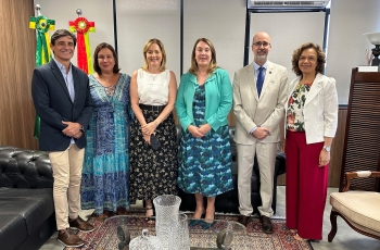 Quatro mulheres e dois homens, todos de pé, posam para a foto em uma pequena sala com bandeiras do Brasil e de SC ao fundo