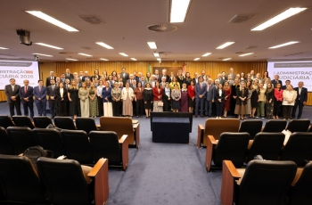 Cerca de 50 pessoas posam para a foto em pé, à frente de um auditório