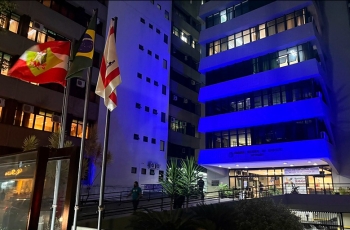 Foto mostra cinco pavimentos do prédio-sede do TRT-SC, iluminado de azul escuro, em ângulo inclinado