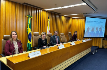 Foto de uma mesa de honra com três mulheres e um homem, em um palco de evento