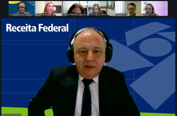 Print de tela de um homem grisalho de terno e gravata fazendo uma palestra por videoconferência