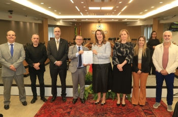 Cinco homens e três mulheres em pé, em uma sala de sessões de julgamento, posam para a foto. Uma mulher e um homem no centro exibem um documento.