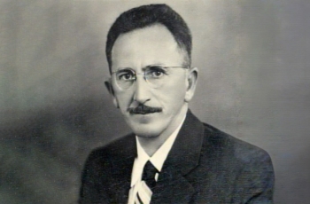 Foto preta e branca de um homem de óculos e bigode