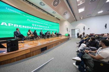 Fotografia de auditório com painel sobre aprendizagem profissional e plateia assistindo.