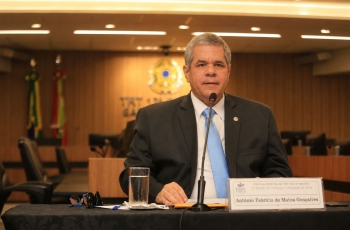 Fotografia de homem sentado falando em uma mesa de honra, durante uma palestra