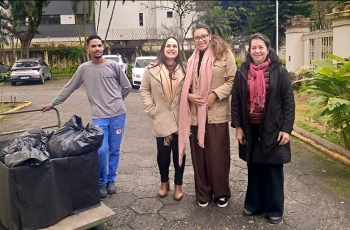 Três mulheres e um rapaz posam para foto ao lado de um carrinho de transporte com sacos pretos