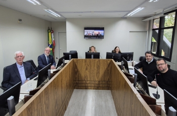 Quatro homens e duas mulheres posam para a foto, sentados ao redor de uma mesa em formato de U