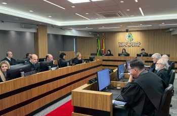 Trezes pessoas vestindo toga sentadas em fileiras de bancadas de madeira, em uma sala de julgamento