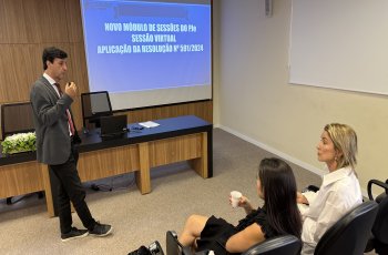 Homem de terno cinza faz uma apresentação a duas mulheres sentadas em um auditório