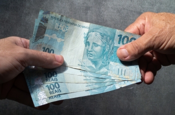 Mão recebe cédulas de 100 reais de outra mão