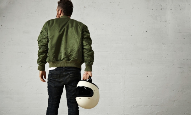 Homem de costas vestindo jaqueta verde e com capacete branco na mão