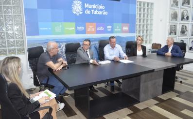 fotografia com uma mesa de reunião no centro. em volta dela seis pessoas conversam sentadas, quatro homens e duas mulheres