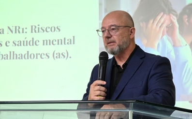 Homem vestindo terno e usando óculos fala ao microfone