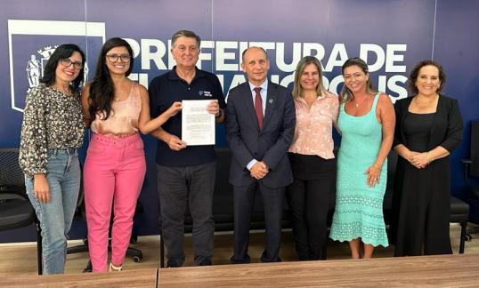 Grupo de pessoas, a maioria mulheres, posa para a foto segurando um documento em papel