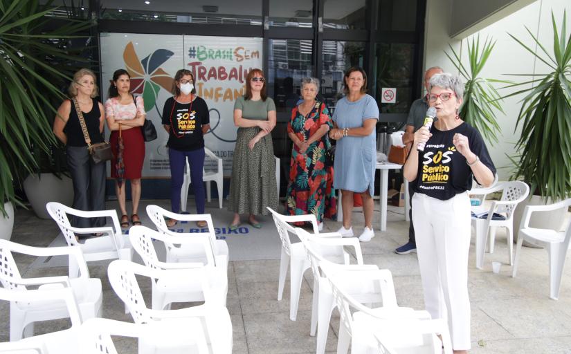 Mulher discursando com camiseta onde se vê escrito SOS serviço público