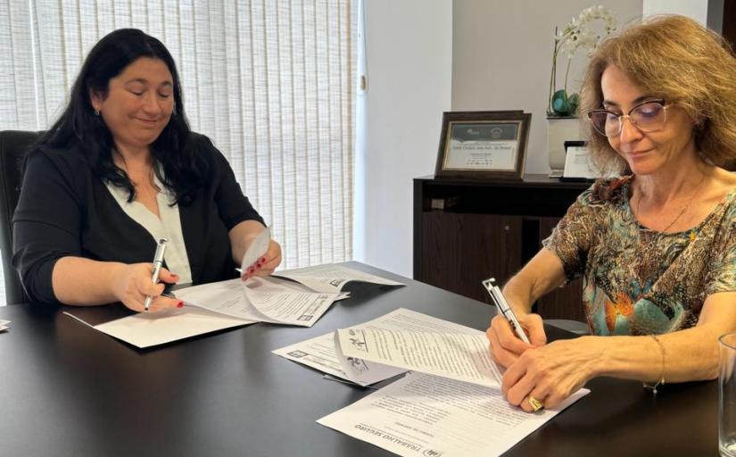 Duas mulheres sentadas em frente a uma mesa preta assinando papéis