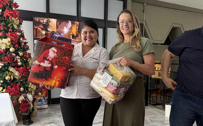 Duas mulheres sorriem para a foto. Uma delas segura uma cesta de Natal e a outr auma cesta básica de alimentos.