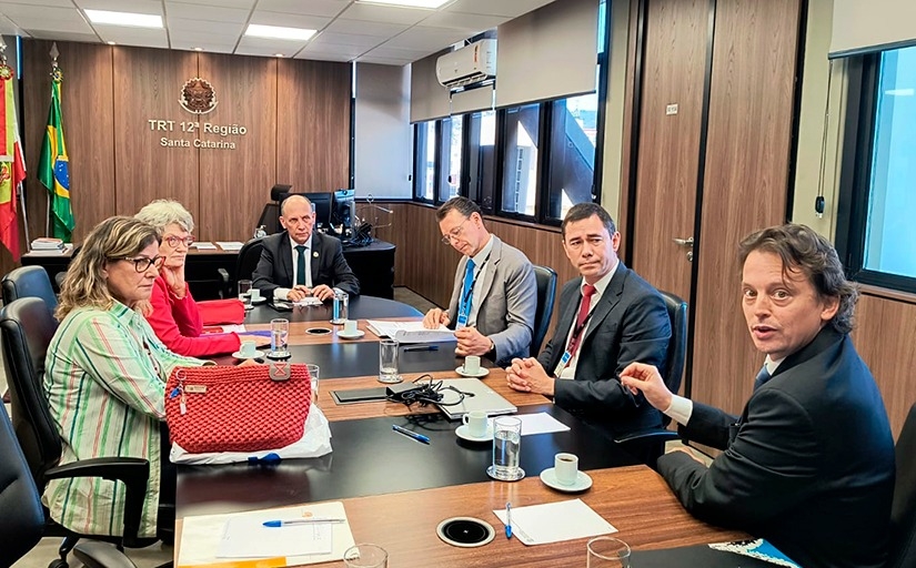Duas mulheres e quatro homens estão sentados em uma mesa oval de reunião
