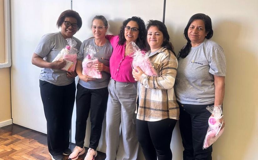 Cinco mulheres estão em pé, sorrindo e posando para a foto
