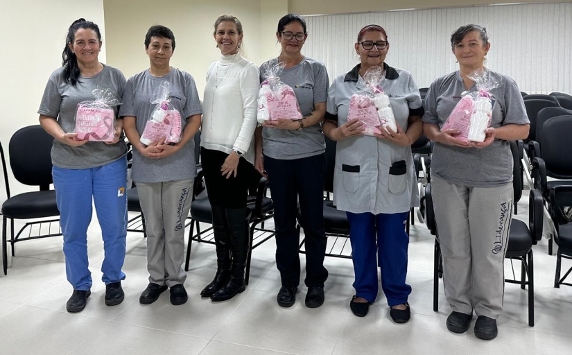 Grupo de seis mulheres. Cinco delas seguram um kit com squeeze e camiseta do Outubro Rosa