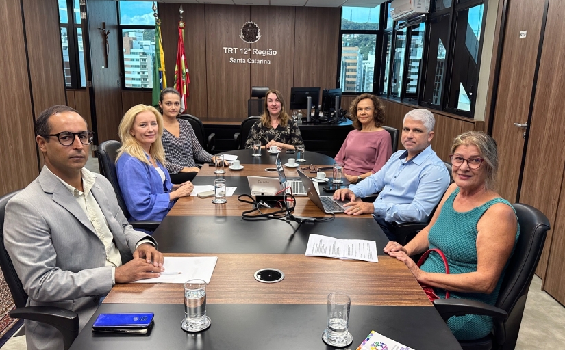 Dois homens e quatro mulheres estão sentados em uma mesa oval de reunião