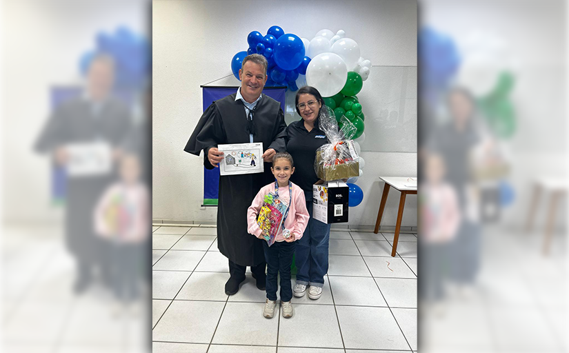 Homem de toga, mulher e menina com medalha e presente posam em cerimônia com balões