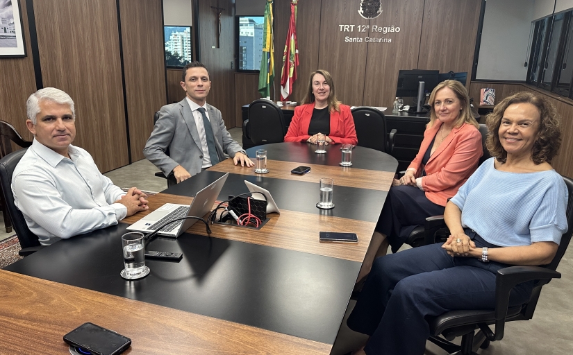 Dois homens e três mulheres estão sentados em uma mesa oval de reunião